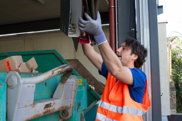 Worker at a waste container throwing away folders in a dumpster rental in Lott TX